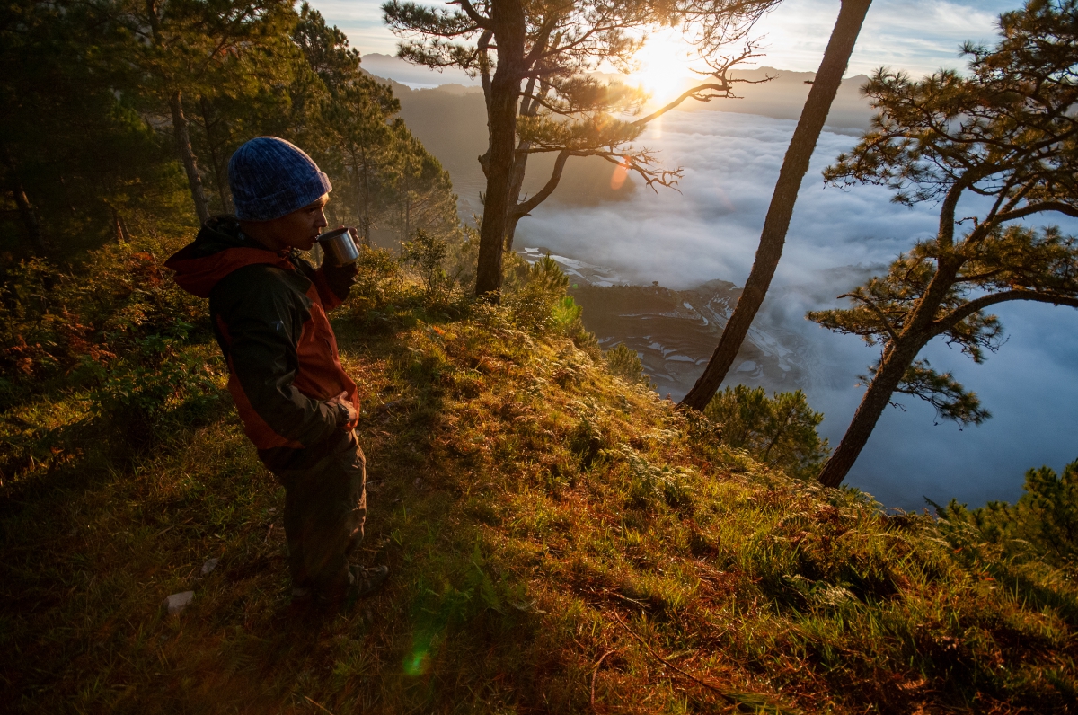 Uncharted Adventure Travel's president, Leo Cuesta, sips some morning coffee at a mountain camp site while looking over a sea of clouds rolling over the valley below.