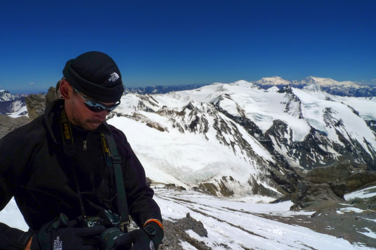 Photographer Zean Villongco holding on to his camera while standing amidst a background of snowy mountains.